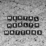 Black letter tiles spelling Mental Health Matters on a speckled grey stone surface